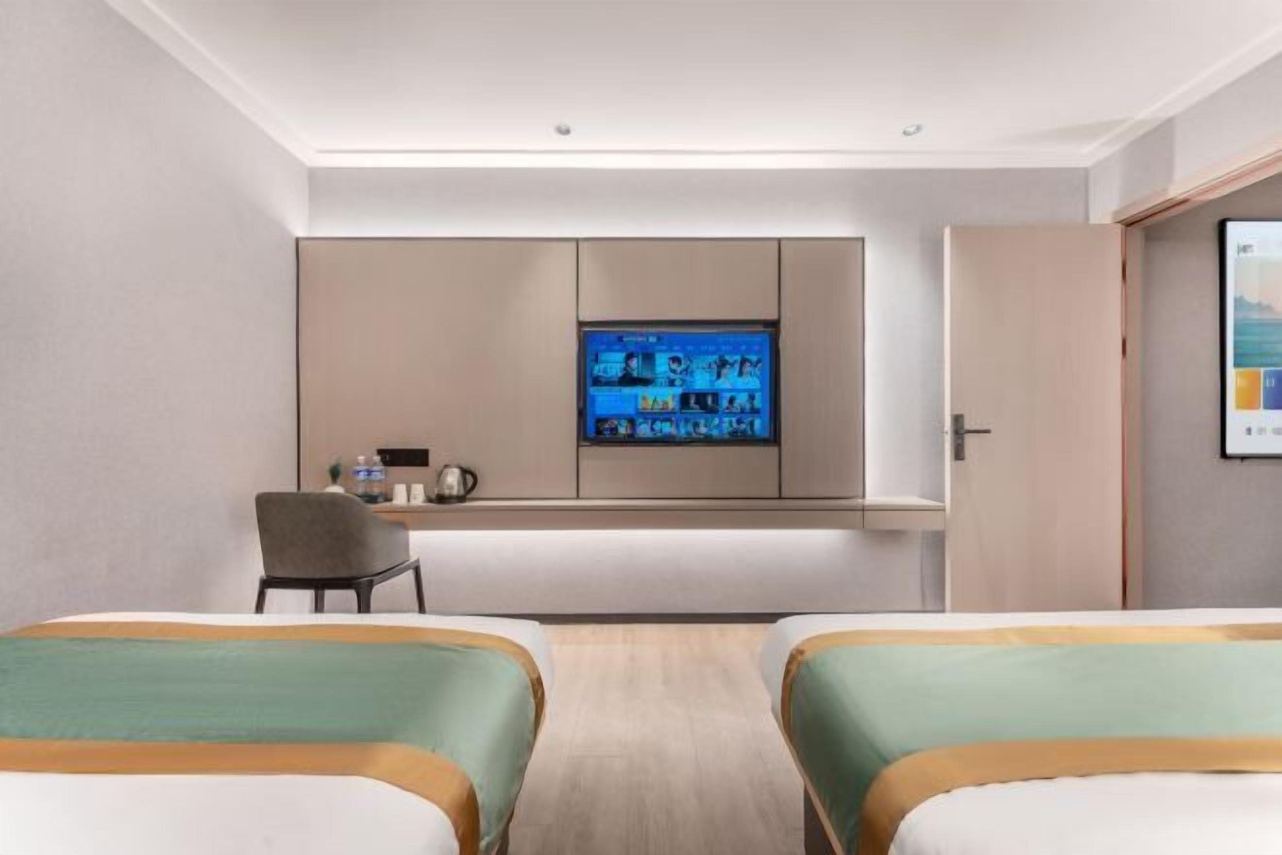 A hotel room with two beds, a desk with a computer, a television, and a door.