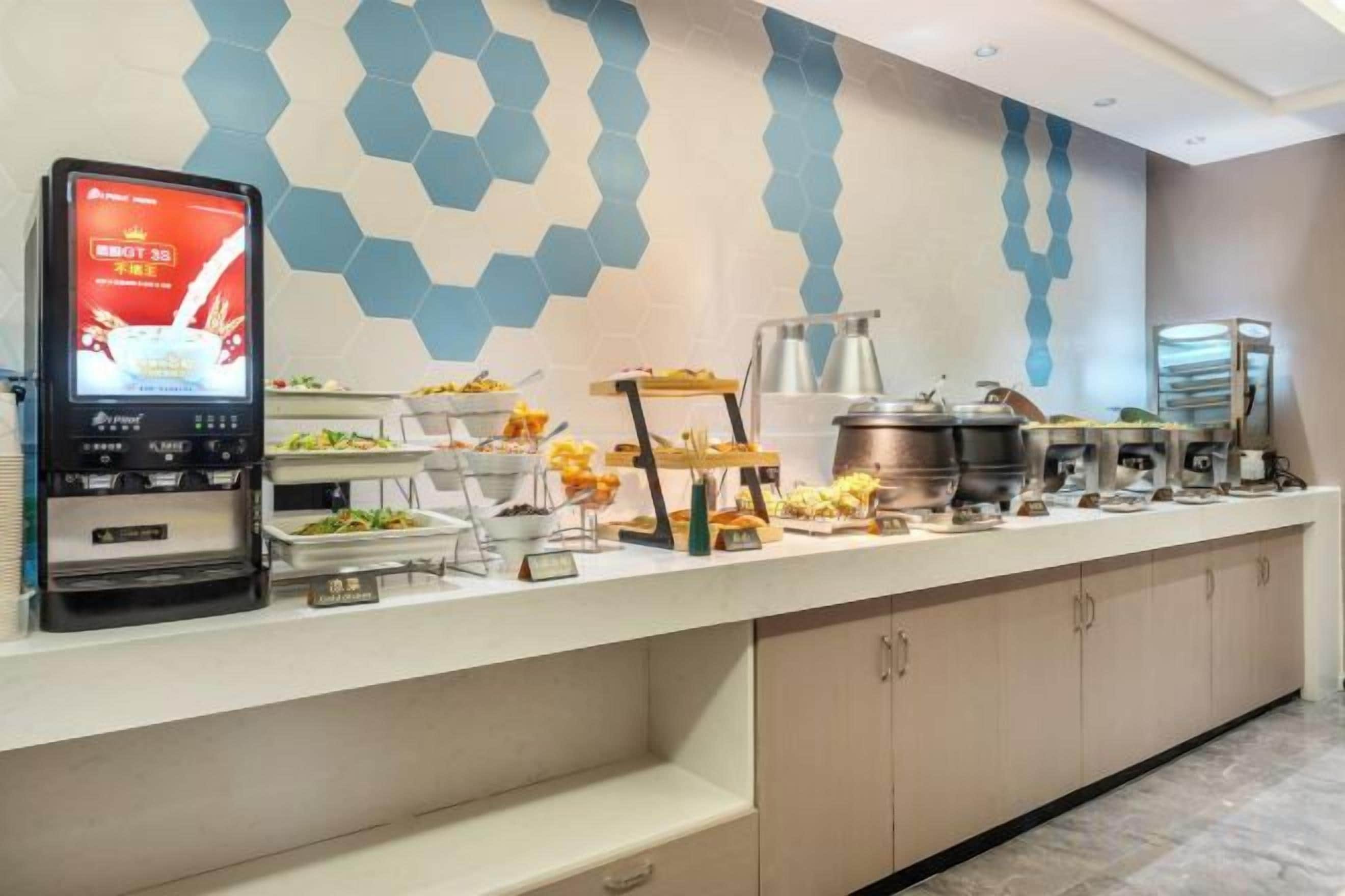 A buffet setup with a digital menu display, various food stations, and a modern geometric wall design.