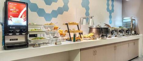 A buffet setup with a digital menu display, various food stations, and a modern geometric wall design.