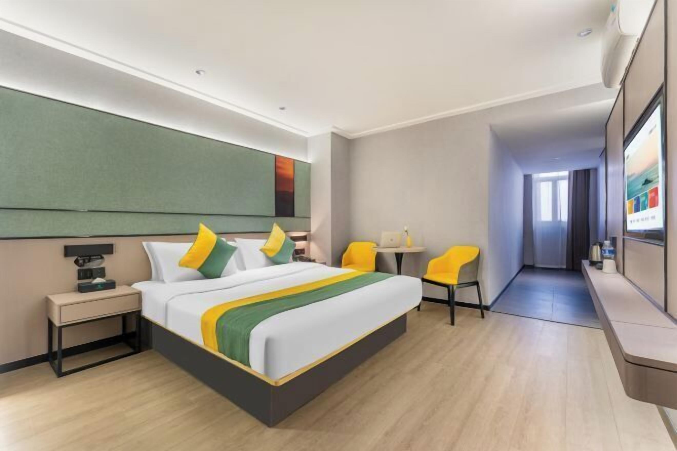 A hotel room with a bed, bedside table, chairs, a desk, and a TV.
