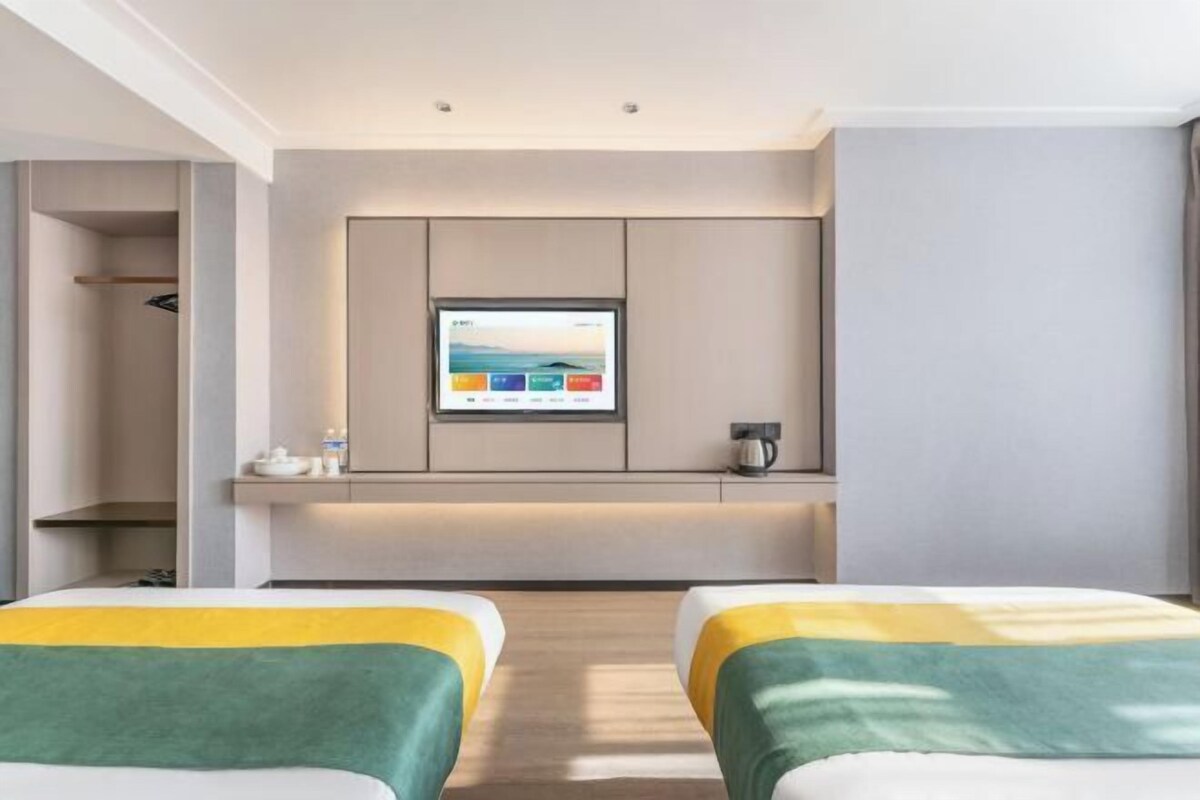 Ein Hotelzimmer mit zwei Betten, einem Fernseher an der Wand, einem kleinen Tisch und einem Kleiderschrank.