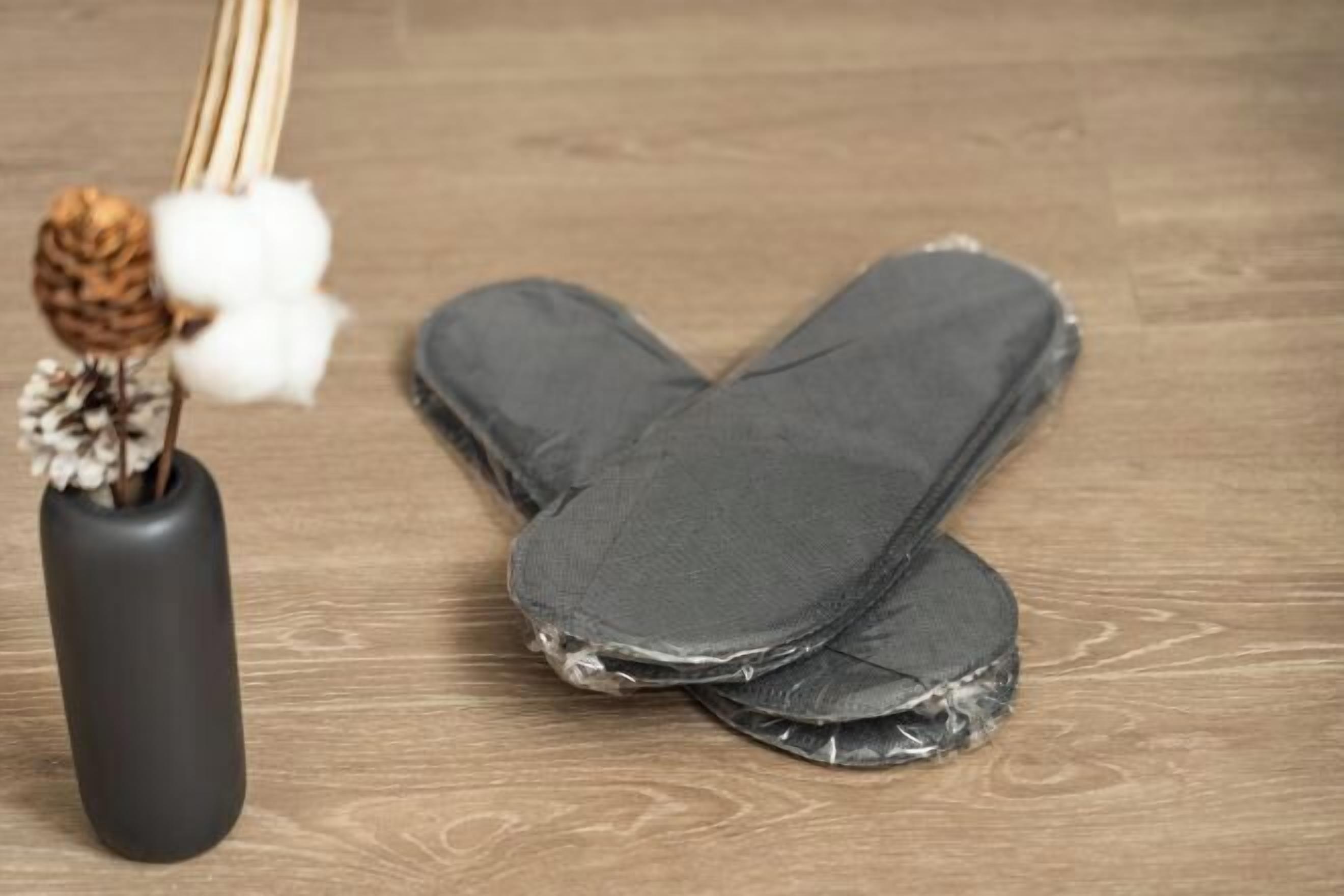 Un par de jeans sobre un piso de madera, con un jarrón negro y flores secas.