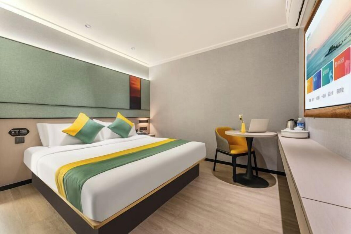 Ein modernes Hotelzimmer mit einem großen Bett, einem Schreibtisch mit Stuhl und einem an der Wand befestigten Fernseher.