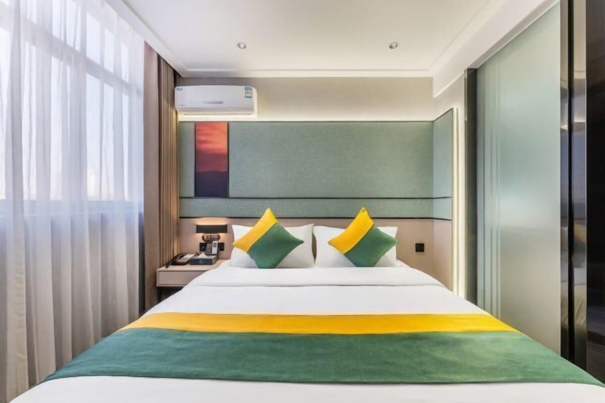 Ein Hotelzimmer mit Bett, Nachttisch, Lampe und einem Fenster mit Vorhängen.