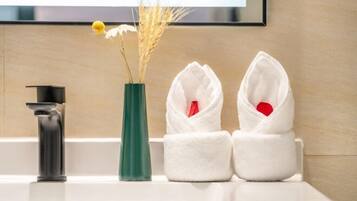 A bathroom with a sink, a green vase with dried flowers, and two white towels with red heart-shaped tags.