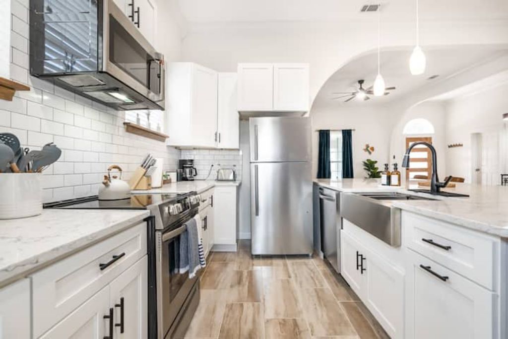 A modern kitchen with white cabinets, stainless steel appliances, and a marble countertop.