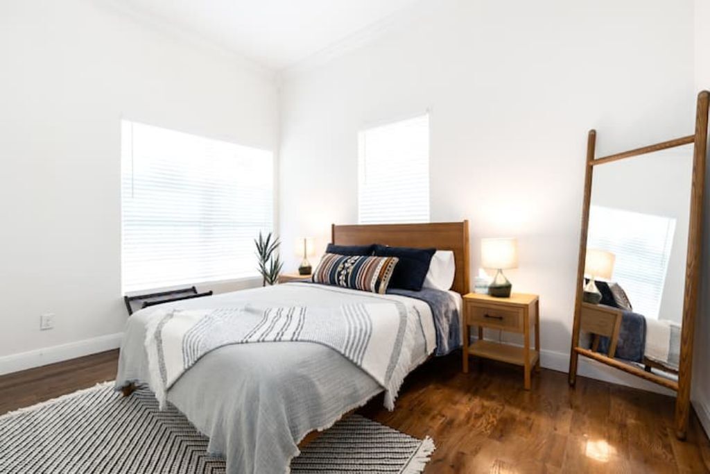 A bedroom with a bed, bedside tables, a mirror, and a window with blinds.
