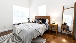 A bedroom with a bed, bedside tables, a mirror, and a window with blinds.