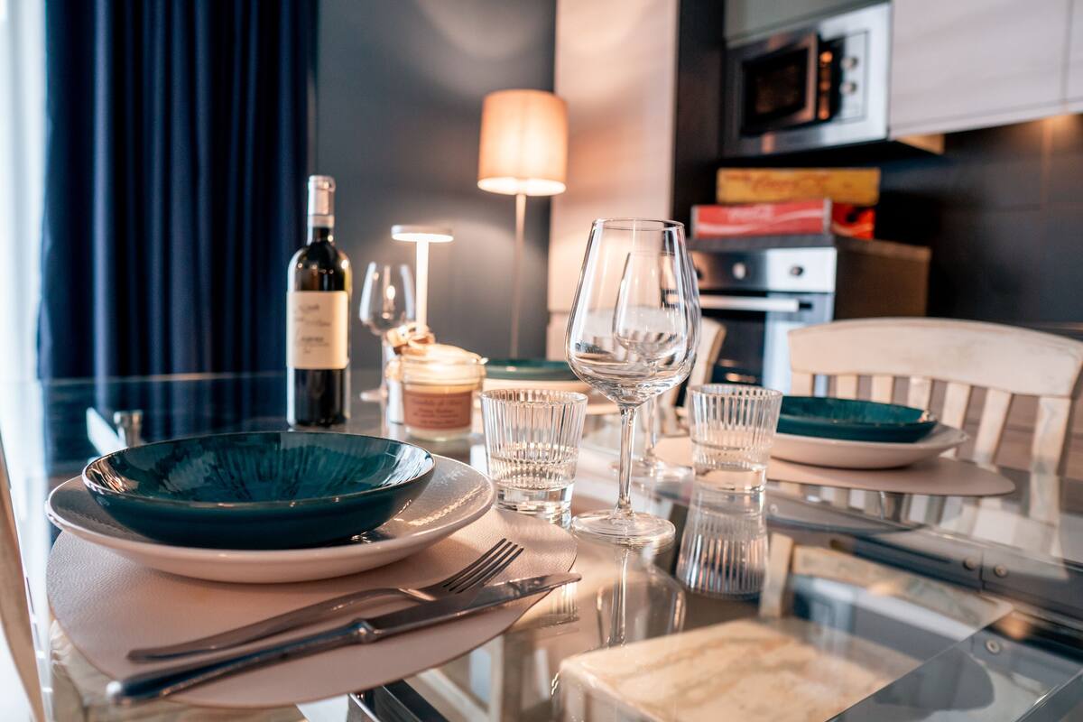 A dining table set with plates, cutlery, and glasses, with a bottle and candle in the background.