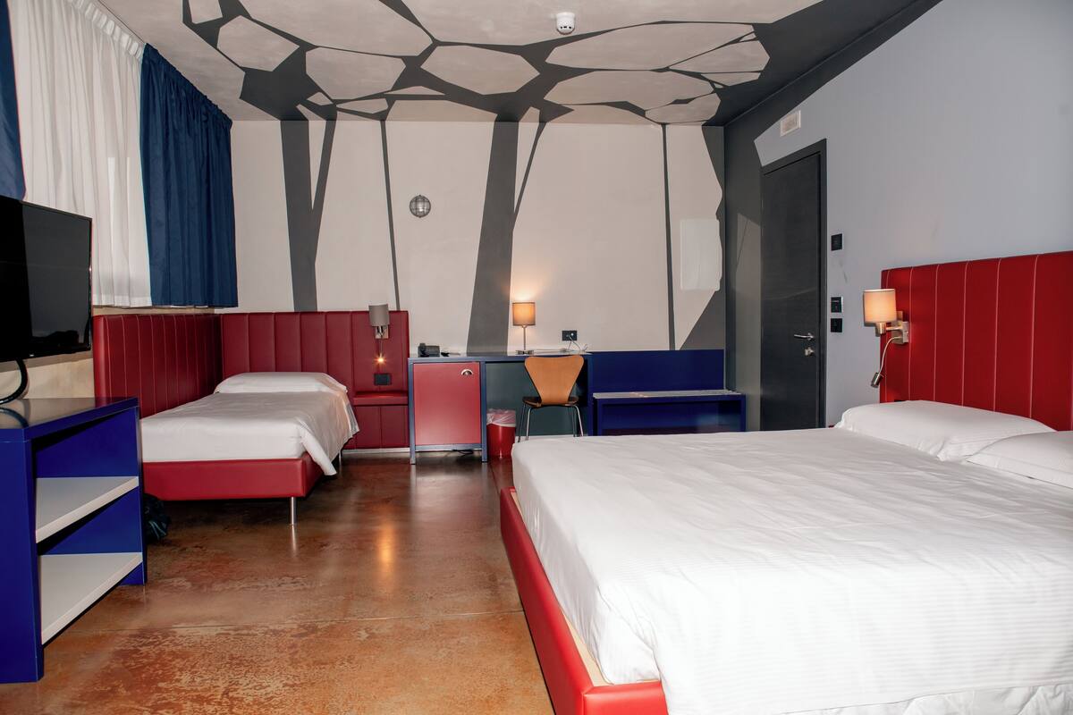 A hotel room with two beds, a desk, a chair, a TV, and a wardrobe.
