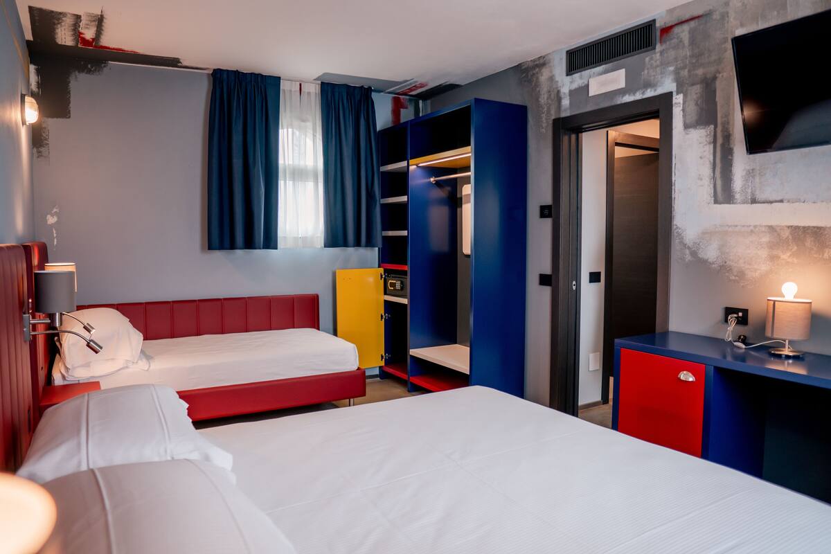 A hotel room with two beds, a wardrobe, a desk, and a TV.