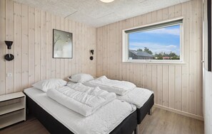 Un dormitorio con dos camas, una ventana con vistas, una lámpara de pared y un cuadro enmarcado.