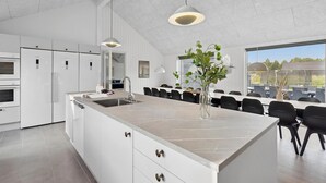 A modern kitchen with white cabinetry, a large island with a sink, and pendant lighting. - Gorgeous home in Rømø with sauna (Rømø)