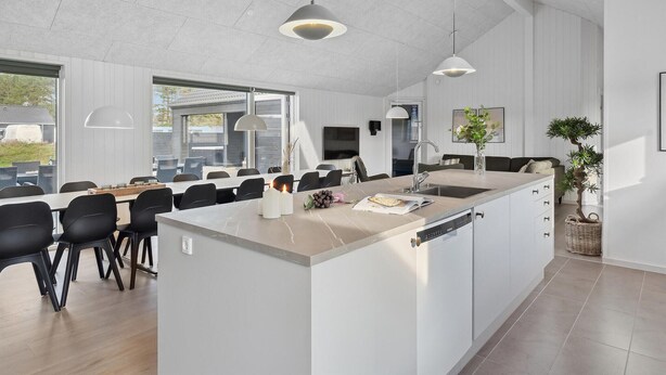A modern kitchen with a large island, pendant lighting, and a dining area with black chairs. - Gorgeous home in Rømø with sauna (Rømø)
