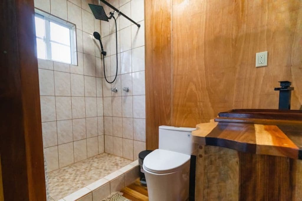 A bathroom with a wooden vanity, a shower with a handheld showerhead, and a toilet.