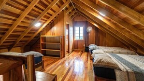 Une chambre mansardée avec des poutres en bois, une fenêtre, un ventilateur et deux lits.