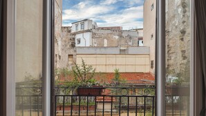 A view through a window with a metal railing, featuring a courtyard with plants and a building with a red-tiled roof. - Marina Square Open Space (Palermo)