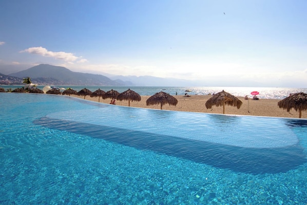 Une piscine d’eau cristalline, avec une plage et des montagnes en arrière-plan.