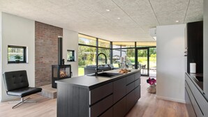 A modern kitchen with a central island, a brick accent wall, and large windows offering a view of the outdoors. - Gorgeous home in Skibby with kitchen (Skibby)