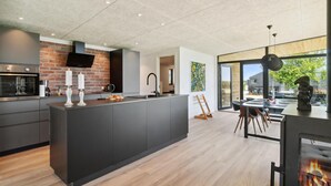 A modern kitchen with a large island, a brick accent wall, and a dining area with a view. - Gorgeous home in Skibby with kitchen (Skibby)