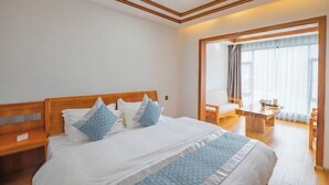A hotel room with a large bed, a wooden headboard, a small table, and a view of the outdoors through a window. - Jiayuan Boutique Hotel (Gongshan)