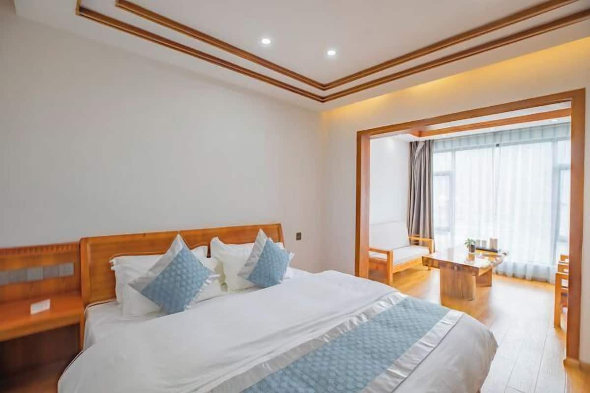 Ein Hotelzimmer mit einem großen Bett, einem hölzernen Kopfteil, einem kleinen Tisch und Blick ins Freie durch ein Fenster.