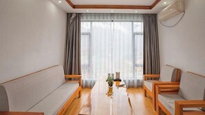 A modern room with a wooden table, two sofas, a large window with curtains, and an air conditioning unit. - Jiayuan Boutique Hotel (Gongshan)