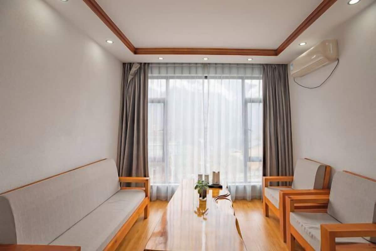 Ein modernes Zimmer mit einem Holztisch, zwei Sofas, einem großen Fenster mit Vorhängen und einer Klimaanlage.