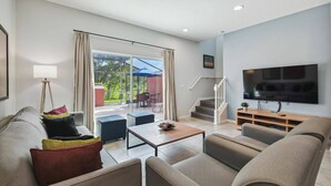 Un salon moderne avec un canapé, une table basse et un téléviseur. Un escalier mène à un espace extérieur aménagé avec une table et des chaises.