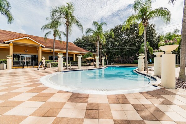 A swimming pool with a tiled deck, palm trees, and a building with a yellow facade. - Encantada 2-Suite Home Near Disney w/ Free Hot Tub (Kissimmee)