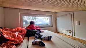 A room with a bed, a window with a view of trees and a cloudy sky, and a door with a vent. - Exclusive House with old Mountain-Railway (Baden-Baden)