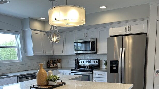 A modern kitchen with a large island, stainless steel appliances, and bar stools. - Peaceful Condo (Grand Haven)