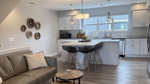A modern kitchen with white cabinets, a central island, and a dining area with a sofa and coffee table. - Peaceful Condo (Grand Haven)