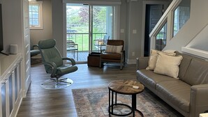 A spacious living room with a sofa, a chair, a coffee table, and a view of the outdoors through a sliding glass door. - Peaceful Condo (Grand Haven)