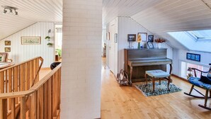 Amplia sala de estar con una escalera de madera, un piano y un sillón mecedor.