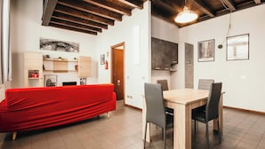 A modern dining area with a wooden table and chairs, a red sofa, and a kitchen area with cabinets and a hanging light fixture.