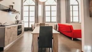 A modern kitchen with a dining area, large windows, and a red sofa.