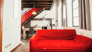A modern living space with a red sofa, a staircase, a kitchen area, and a dining table.