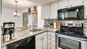 A modern kitchen with white cabinets, a stainless steel microwave, an oven, a dishwasher, and a granite countertop. - Deer Ridge Resort C207 - Amazing Mountain Views, Pool, and Tennis (Gatlinburg)