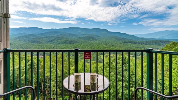 A balcony with a view of green mountains, a table with two mugs, and a 'No Grilling or Smoking' sign. - Deer Ridge Resort C207 - Amazing Mountain Views, Pool, and Tennis (Gatlinburg)