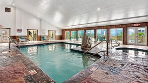 An indoor swimming pool with clear water, surrounded by lounge chairs and a view of the outdoors. - Deer Ridge Resort C207 - Amazing Mountain Views, Pool, and Tennis (Gatlinburg)
