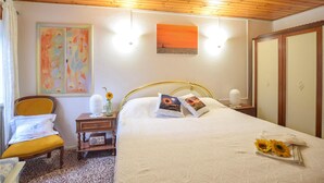 Ein Schlafzimmer mit Bett, Sessel, Nachttisch, Radio und einem Bild an der Wand.