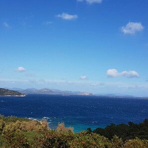 Eine Küstenlandschaft mit blauem Himmel, Blick auf das Meer und entfernten Bergen.