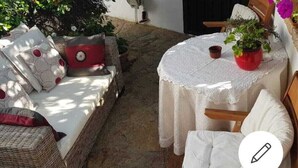 A cozy outdoor seating area with wicker furniture and a round table, surrounded by potted plants and a stone floor. - Vacation Home Il Gelsomino-5 minutes from the beach (Siniscola)