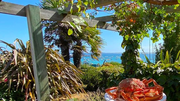 An outdoor dining area with a table set for two, overlooking a coastal view.