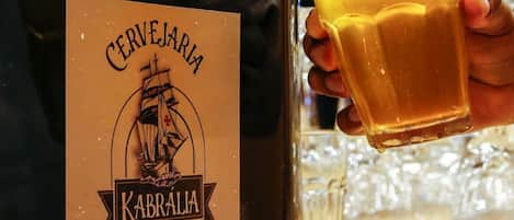 A hand holding a glass of beer next to a bottle labeled 'Cerveja KABRALA Porto Seguro Brasil.'