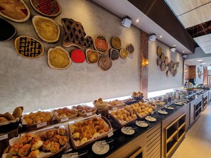 Un bufé con diversas opciones de panadería y una pared decorada con posavasos de madera.