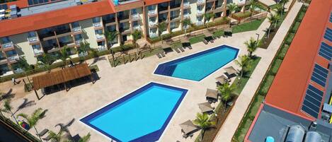 A hotel with two swimming pools, multiple balconies, and a rooftop with solar panels.