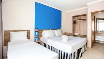 Habitación de hotel con dos camas, cabecero de madera, pared de acento azul, armario de madera y baño con espejo y lavamanos.