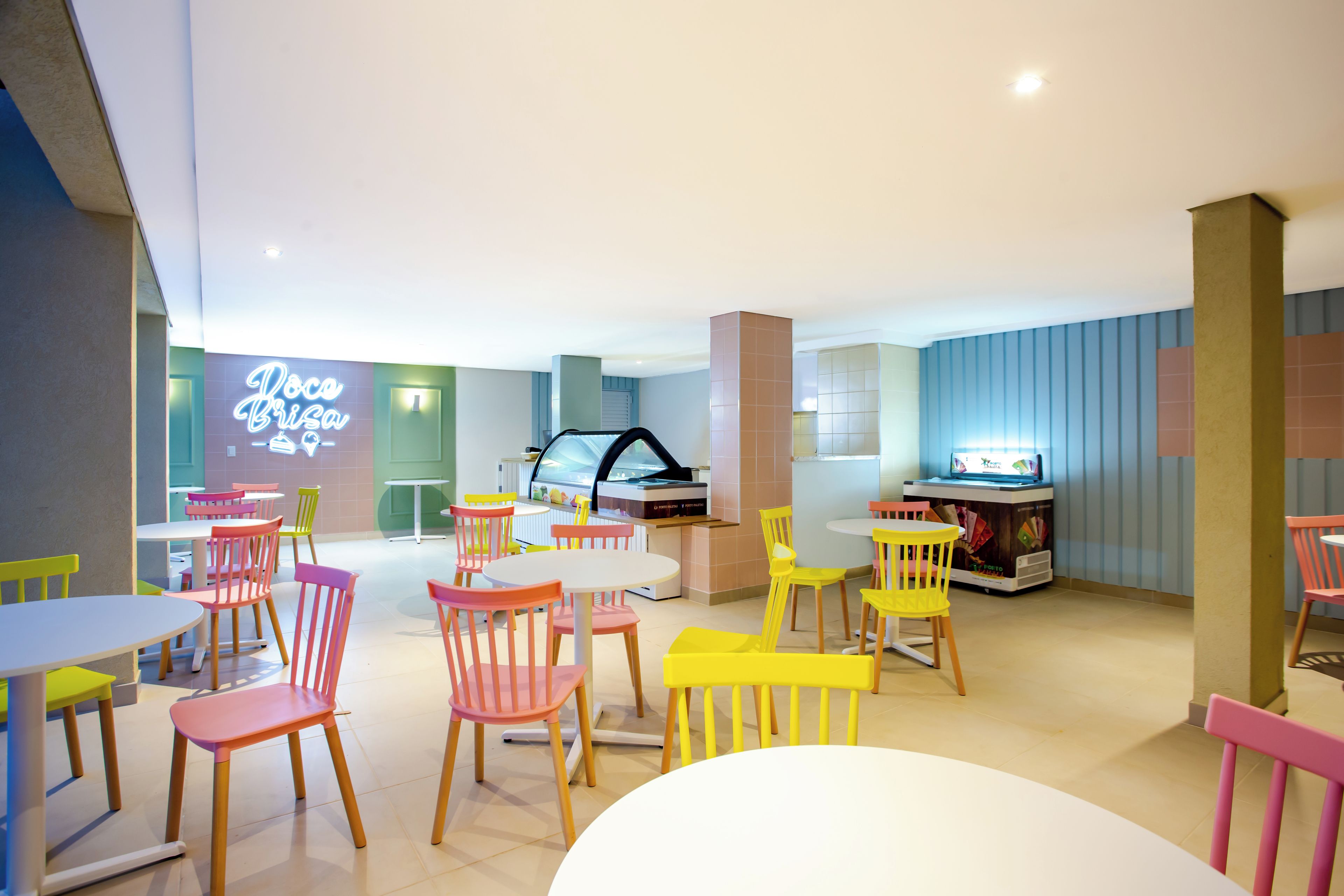 A brightly lit indoor space with multiple tables and chairs, a neon sign, and a vending machine.